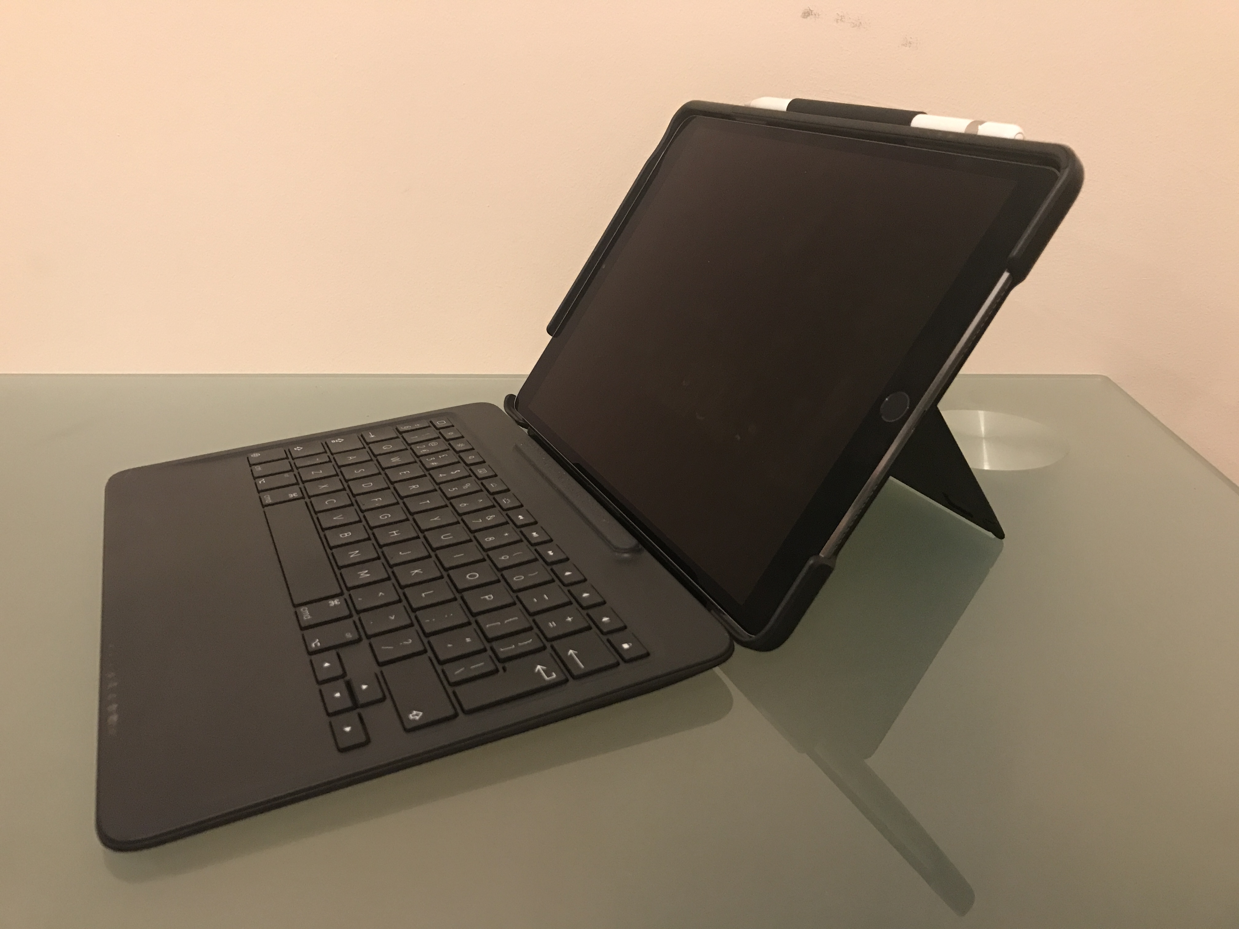 An iPad propped up in the Logitech keyboard case. There's a kickstand behind the iPad itself and the Apple Pencil is held to the top edge with a fabric loop.