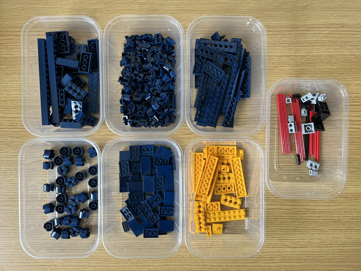 Seven tubs of lego. Five contain blue pieces, one contains yellow pieces, and the last one has a mixture of red, black, and grey pieces.