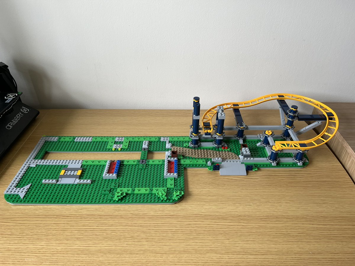 A partially built lego roller coaster with a small curve on track on the right side, and unfinished floor on the left side. It’s so wide that the edges of the desk it’s being built on are visible