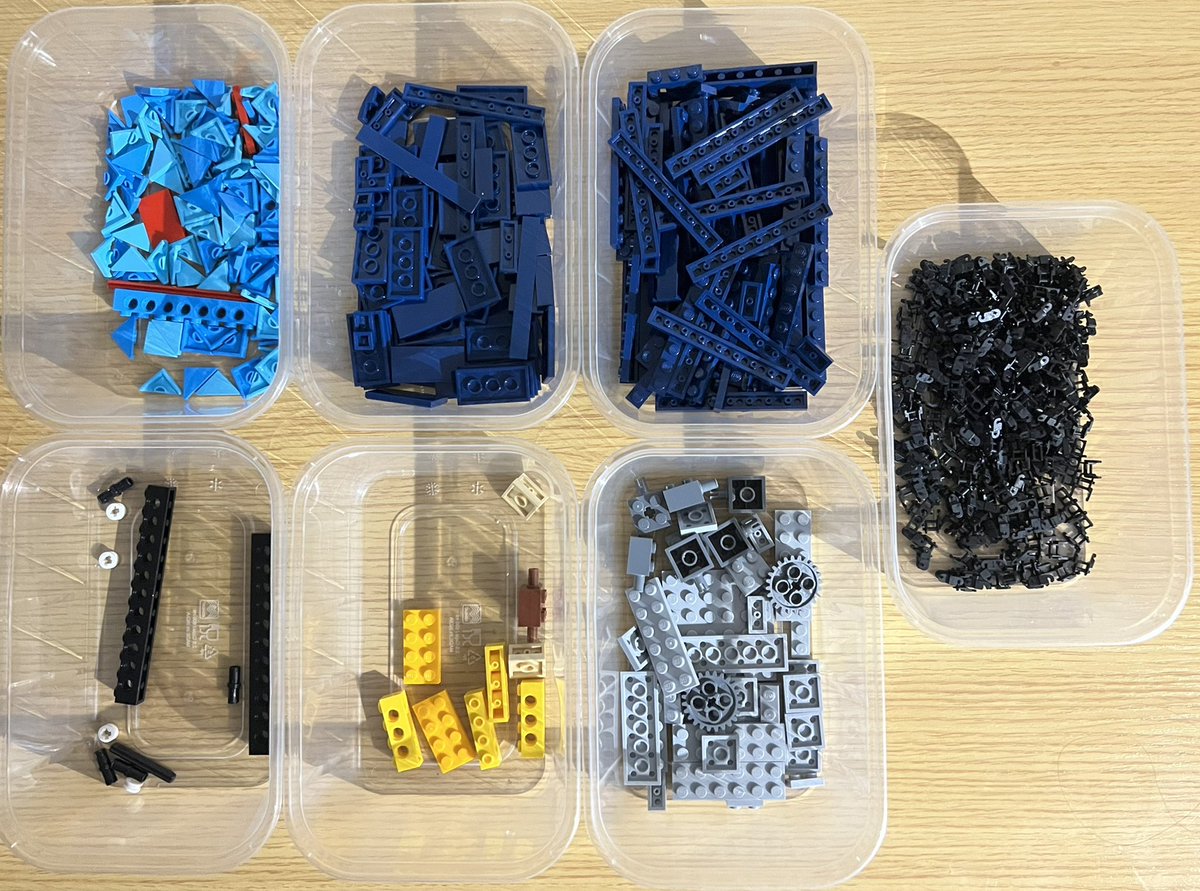 Seven tubs of lego sorted by colour. There are two tubs of dark blue, a tub of light blue, three mixed tubs, and a tub full of black chain link pieces.