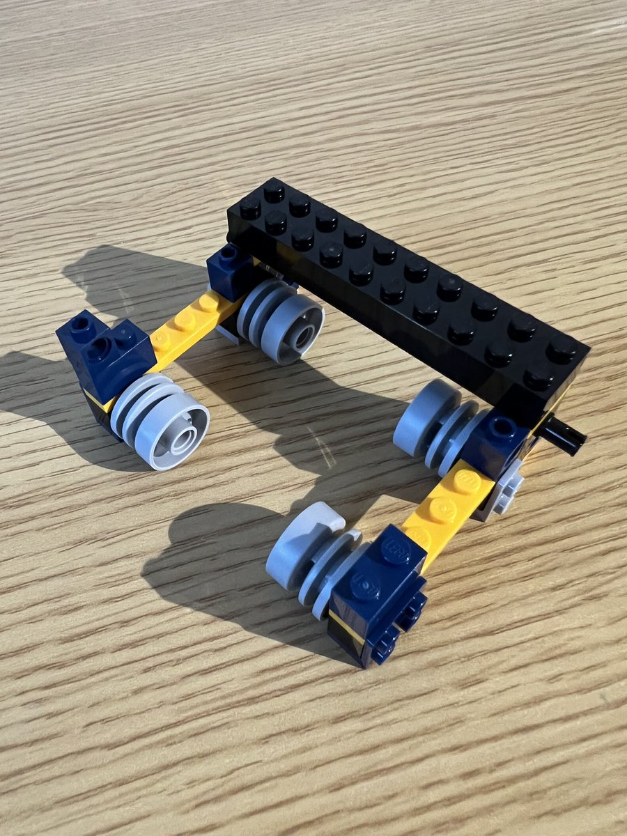 A small lego structure with two thin walls on the sides, a slightly thicker wall at the back, and four wheels on the inside of the walls.