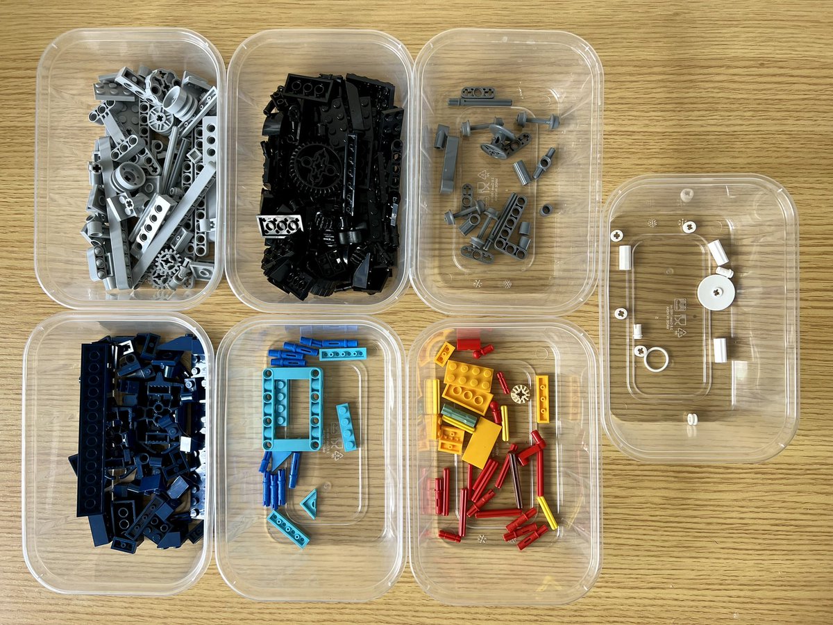 Seven tubs of lego sorted by colour. There are light grey, dark grey, black, and beige coloured wheels of various sizes in the different tubs.