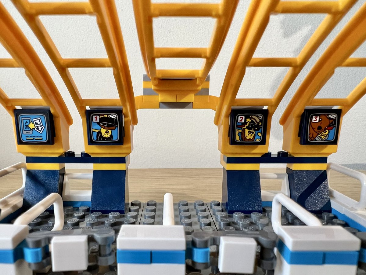 A lego roller coaster station with ride photos displayed on tv screens. One of the photos has someone dropping a hotdog while on the ride, and another has a picture of a squirrel with its nose pressed up against the lens.